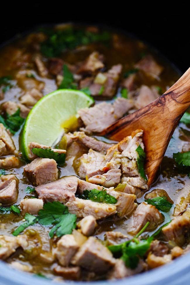 This is easily the BEST chili verde that I have EVER had! The pork is tender and full of amazing flavor and is made right in the slow cooker! Close up photo a pork Chile Verde with a wooden spoon and a fresh cut lime on top.