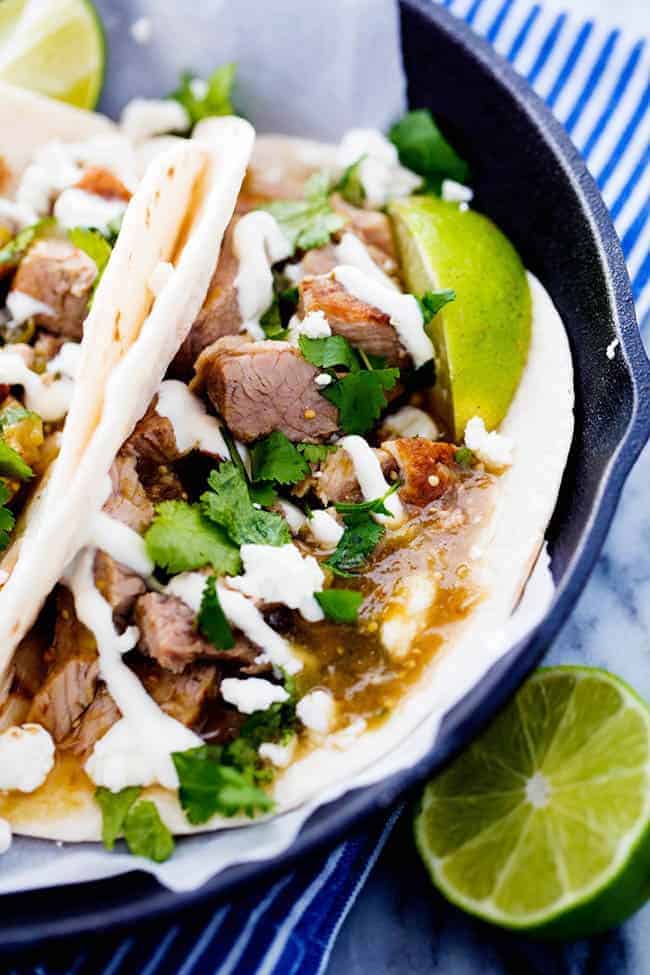 This is easily the BEST chili verde that I have EVER had! The pork is tender and full of amazing flavor and is made right in the slow cooker! Slow Cooker Pork Chili Verde in pita tacos on a black plate with fresh cut limes on the side.
