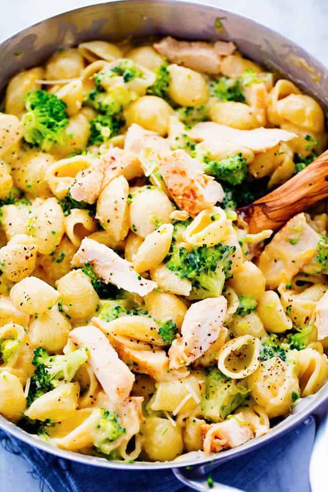 Ditch the boxed mac and cheese and make these amazingly creamy and cheesy chicken broccoli shells. This meal is sure to be a huge hit with the family! CHEESY CHICKEN BROCCOLI SHELLS IN A PAN WITH A WOODEN SPOON.