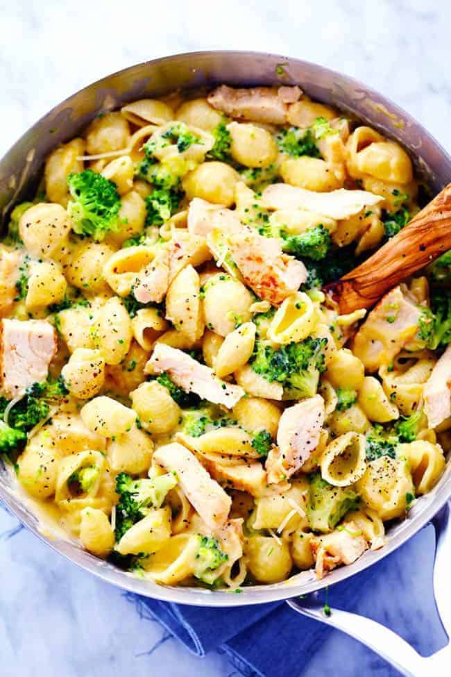 Ditch the boxed mac and cheese and make these amazingly creamy and cheesy chicken broccoli shells. This meal is sure to be a huge hit with the family! CHEESY CHICKEN BROCCOLI SHELLS IN A PAN WITH A WOODEN SPOON.