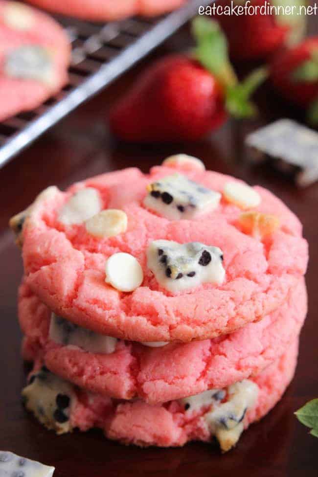 Easy and delicious cookies that are made with a cake mix and pudding mix with delicious cookies and cream pieces hidden inside! They are a fun pink color with a crisp edge and chewy center! Strawberry Cookies 'n Cream Cookies with fresh strawberries in background.