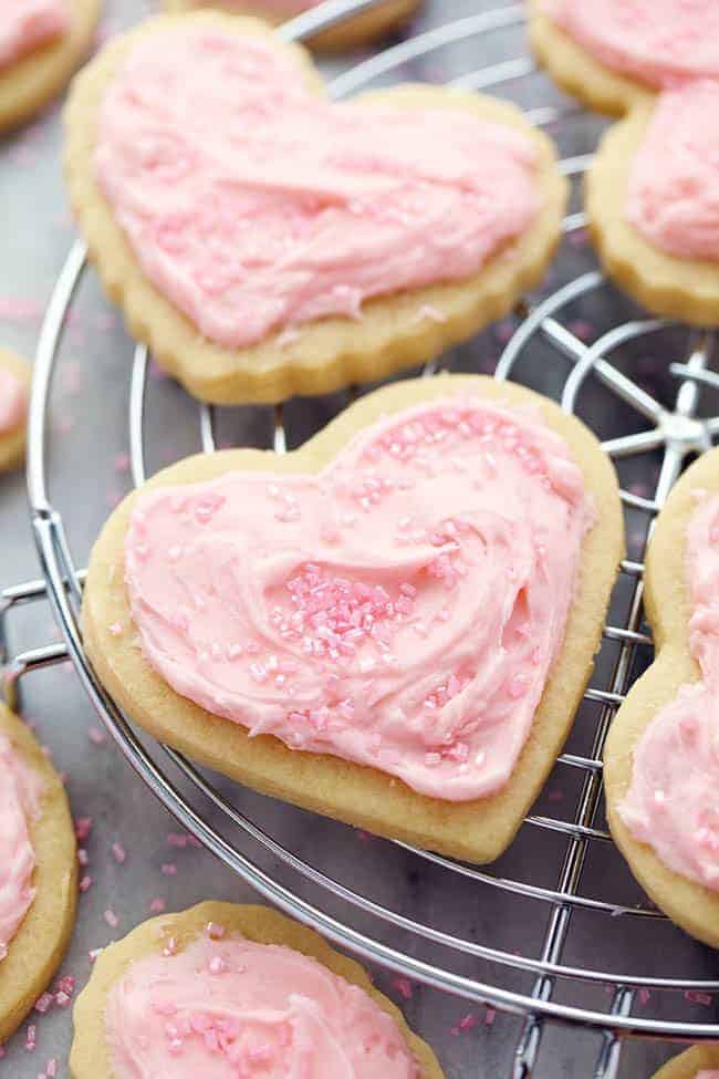 You cannot beat homemade sugar cookies with a crisp edge and a soft center. These are the BEST! Topped with my favorite cream cheese frosting and sprinkles, these sugar cookies are a tried and true favorite. A zoomed in picture of a sugar cookie on a cooling rack.