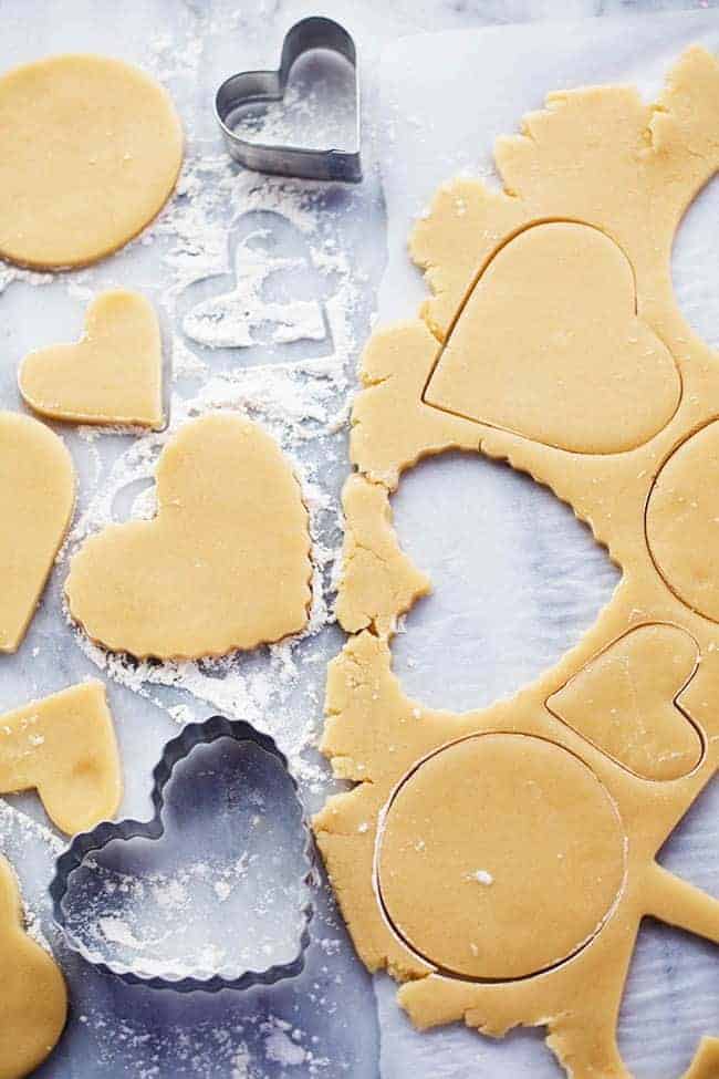 You cannot beat homemade sugar cookies with a crisp edge and a soft center. These are the BEST! Topped with my favorite cream cheese frosting and sprinkles, these sugar cookies are a tried and true favorite. A picture showing how to cut out shapes in the dough.