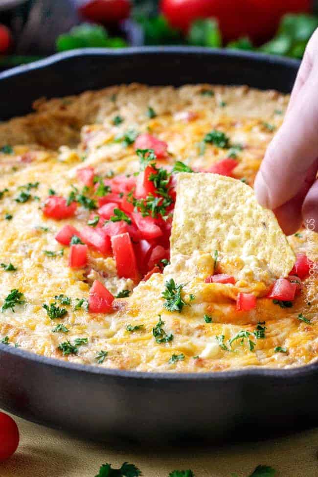 Queso Verde Corn Dip is creamy cheesy, bubbly, packed with flavor and one of the easiest, tastiest appetizers you will ever make! Queso verde corn dip in a large skillet with a chip being dipped into it.