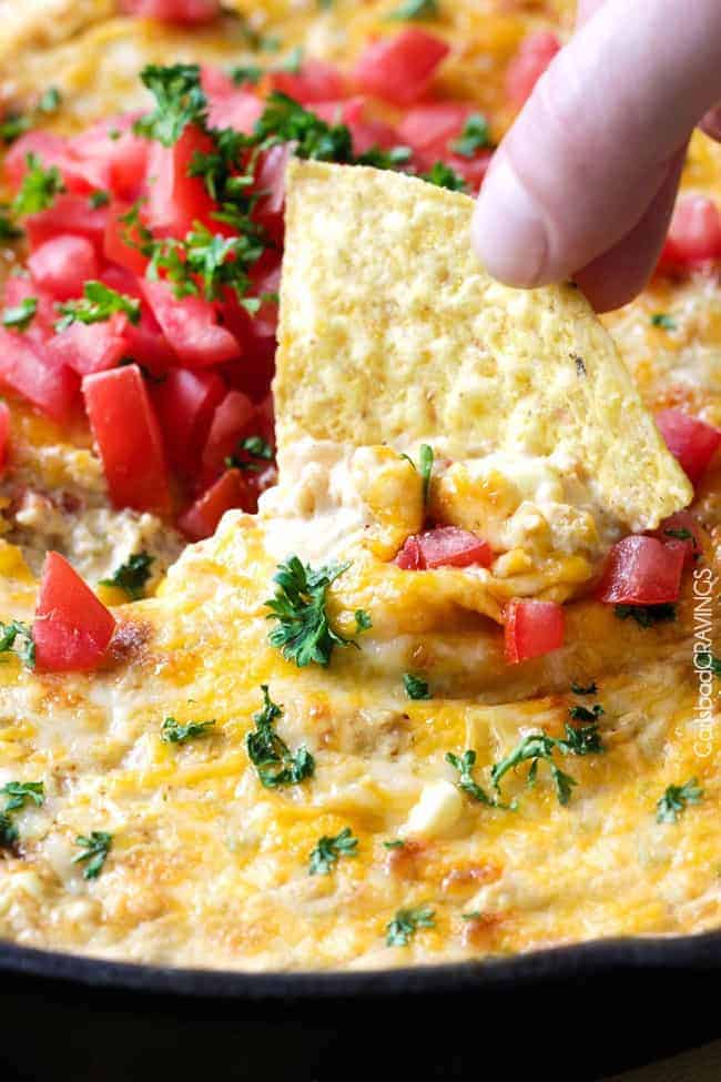 Queso Verde Corn Dip is creamy cheesy, bubbly, packed with flavor and one of the easiest, tastiest appetizers you will ever make! Queso verde corn dip with fresh sliced tomatoes on top with a chip being dipped into it.