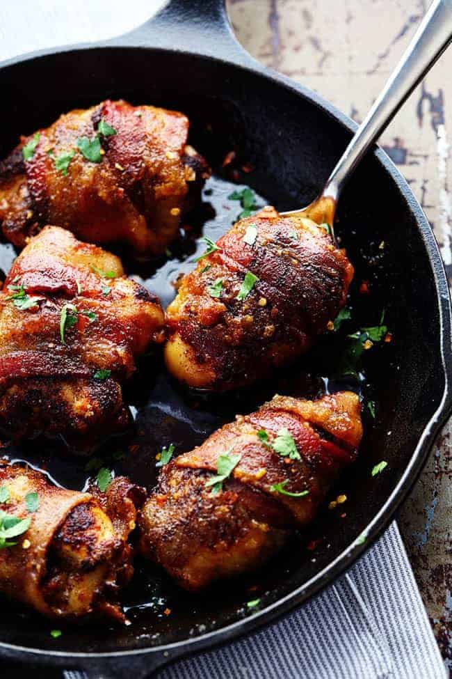 Tender and Juicy Chicken that is wrapped in bacon and coated in a blend of spices. It bakes in brown sugar which caramelizes when it cooks. You are going to love the sweet and spicy flavor! Sweet and spicy bacon wrapped chicken in a skillet with a spoon removing one.