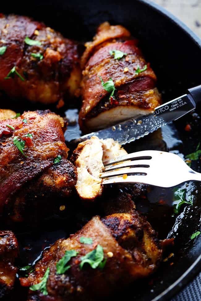 Tender and Juicy Chicken that is wrapped in bacon and coated in a blend of spices. It bakes in brown sugar which caramelizes when it cooks. You are going to love the sweet and spicy flavor! Sweetened spicy bacon wrapped chicken being sliced into with a fork and a knife in a skillet.