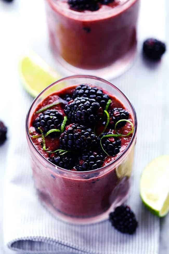 A quick and easy blackberry lime smoothie full of antioxidants and vitamins that your body needs! Up close photo of blackberry lime smoothie in a clear glass with fresh limes and blackberries on the side.