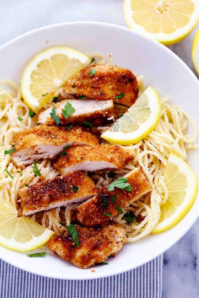 Crispy, tender and juicy parmesan crusted chicken over the most incredible creamy lemon garlic pasta! This is a must make meal! Crispy Parmesan Chicken with Creamy Lemon Garlic Pasta on a white plate with fresh sliced lemons on the side.