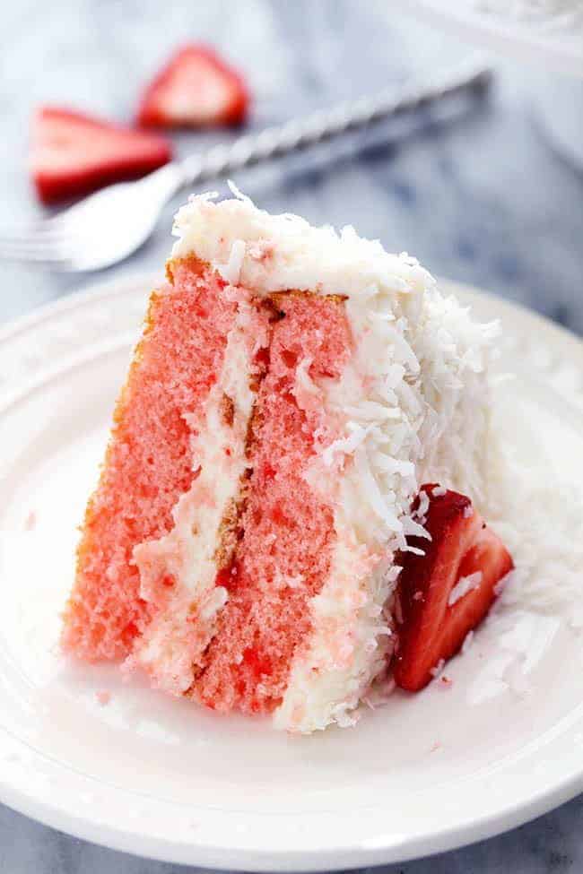 A delicious and moist strawberry coconut cream cake with an amazing coconut cream cheese frosting! A slice of Strawberry Coconut Cream Cake with Coconut Cream Cheese Frosting on a white plate.