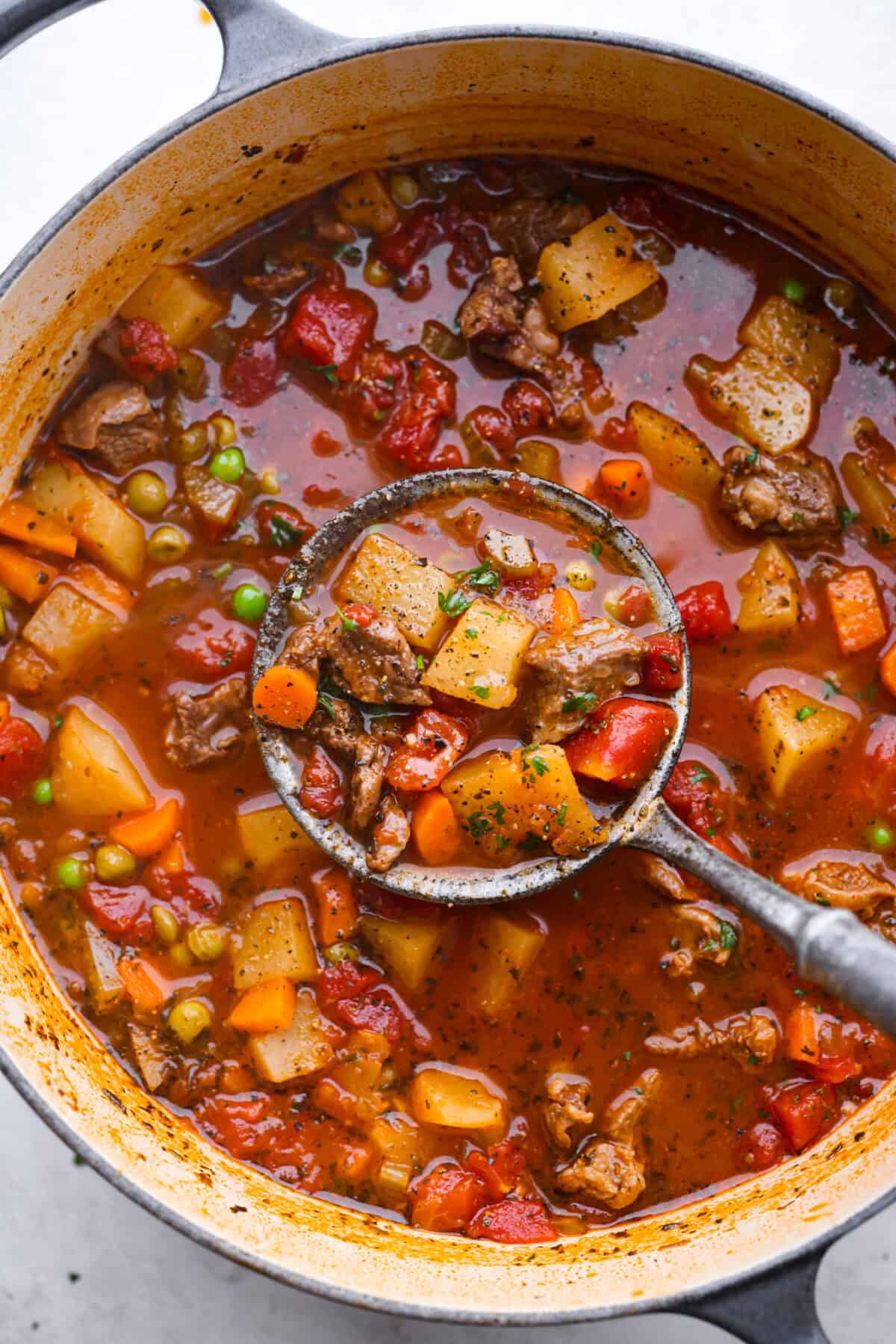 This hearty Vegetable Beef Soup is comforting and flavor-packed! It's loaded with beef, potatoes, and veggies that simmer to tender perfection. A classic and easy one-pot soup for a chilly night. Top view of a ladle lifting vegetable beef soup in a large pot.