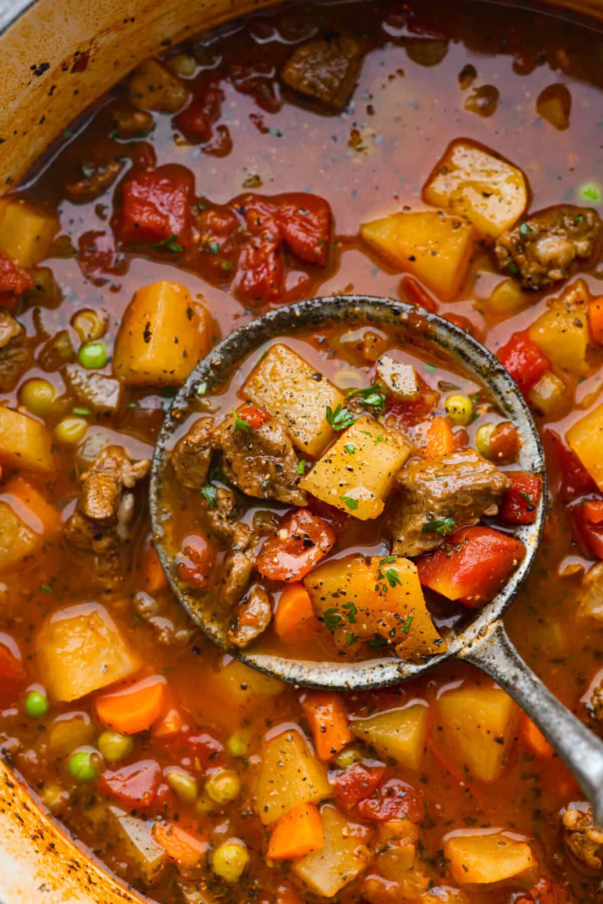 This hearty Vegetable Beef Soup is comforting and flavor-packed! It's loaded with beef, potatoes, and veggies that simmer to tender perfection. A classic and easy one-pot soup for a chilly night. Top close view of a ladle lifting up vegetable beef soup from the pot.