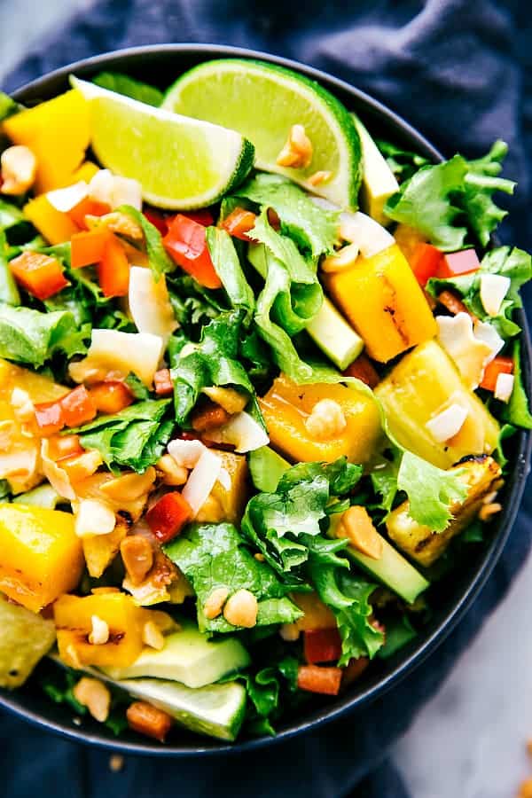 Delicious grilled mango and pineapple tossed in a mouthwatering salad! You will want to make this all summer long! Grilled mango and pineapple salad in a large black bowl.