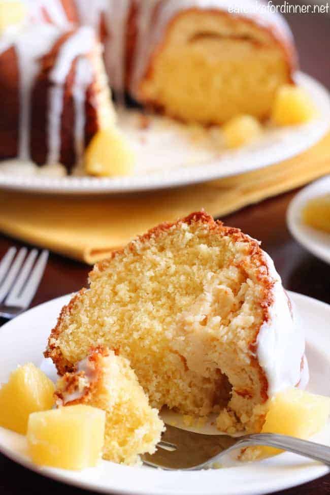 Pineapple has such a mild flavor, so it really helps to serve fresh chopped pineapple with this cake to enhance the pineapple flavor. Give it a try or create your own version. . . it will become a new staple recipe in your house. A slice of Pineapple Cheesecake Cake on a white plate with a metal fork. The rest of the cake is on a white platter in the background.