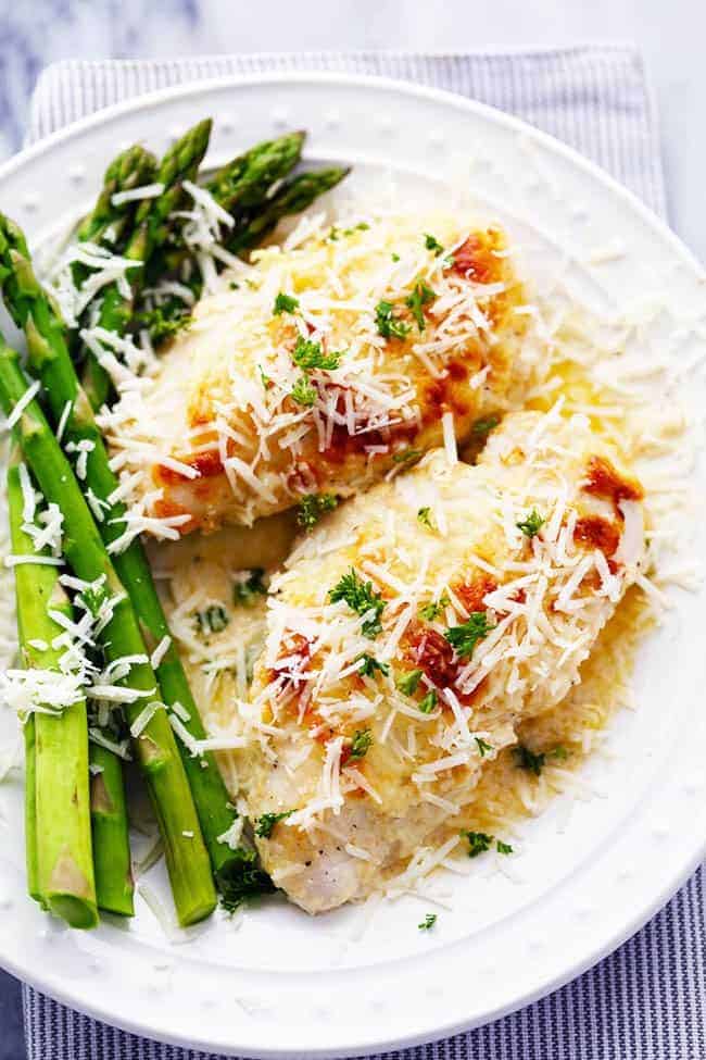 An amazingly creamy baked chicken with asiago cheese inside. It comes together quickly and will be loved by the entire family! Creamy baked asiago chicken and baked asparagus on a white plate.