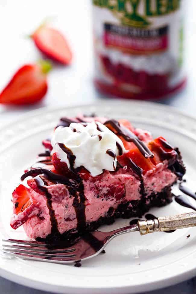 An amazing no bake pie with a chocolate crust filled with a creamy strawberry filling. It gets topped with fresh strawberries and drizzled in chocolate and will be a huge hit wherever it goes!ย A slice of No Bake Chocolate Strawberries and Cream Pie on a white plate with a metal fork.