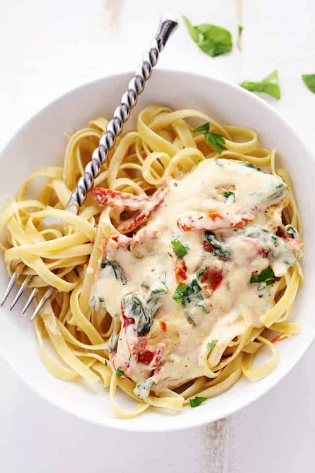 Creamy Tuscan Garlic Chicken has the most amazing creamy garlic sauce with spinach and sun dried tomatoes. This is a restaurant quality meal that's easy to make at home in just 30 minutes! Creamy Tuscan Garlic Chicken over noodles in a white bowl with a metal spoon.