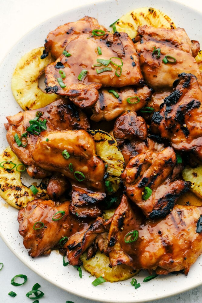 Grilled Huli Huli Chicken is a five star recipe! The marinade is quick and easy and full of such amazing flavor! You will make this again and again! Grilled Huli Huli Chicken on a plate with grilled pineapple and garnished with green onions.