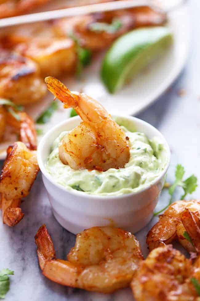 Grilled Spicy Lime Shrimp with Creamy Avocado Cilantro Sauce has a simple but full of flavor and spice marinade. The creamy avocado cilantro sauce is the perfect cool and creamy dipping sauce. Grilled Spicy Lime Shrimp with Creamy Avocado Cilantro Sauce on a table.