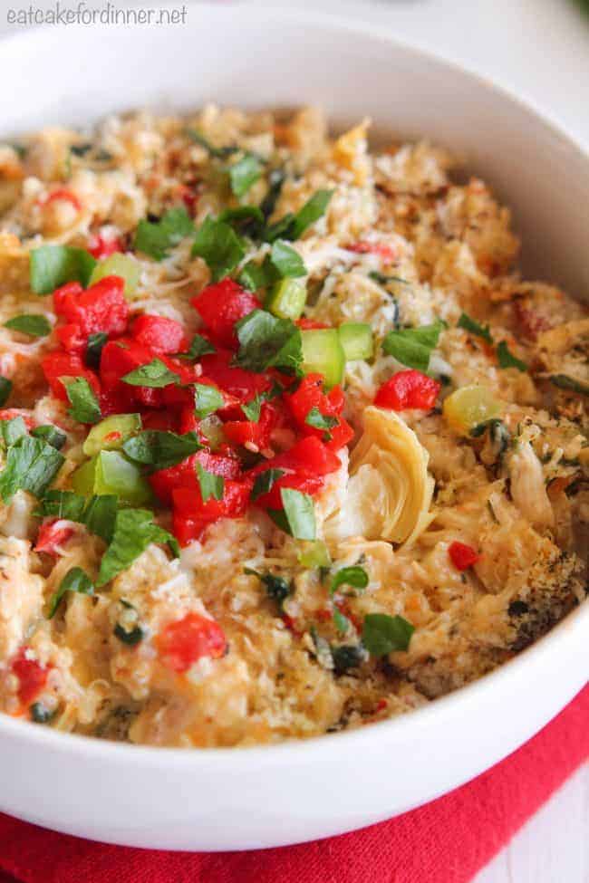 A delicious and healthy meal full of quinoa,ย red pepper, artichokes, spinach, chicken and Greek yogurt. It has such amazing flavors and is a delicious dinner idea! Creamy Spinach and Artichoke Chicken Quinoa in a white bowl.