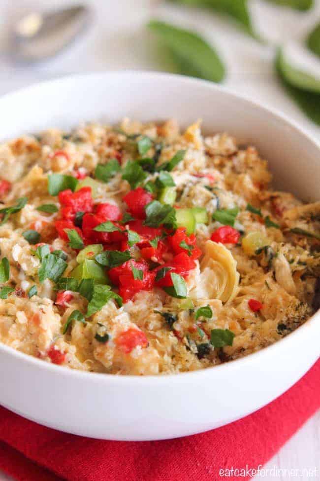 A delicious and healthy meal full of quinoa,ย red pepper, artichokes, spinach, chicken and Greek yogurt. It has such amazing flavors and is a delicious dinner idea! Close up of Creamy Spinach and Artichoke Chicken Quinoa in a white bowl.
