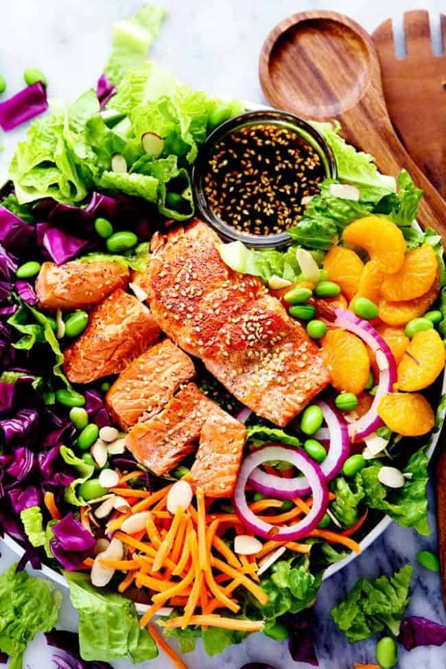 Asian Pan Seared Salmon Salad is bright and vibrant and complete with an amazing honey sesame dressing that takes this salad to a whole new level of delicious! Overhead photo of Asian Pan Seared Salmon Salad in a large bowl with wooden tongs.