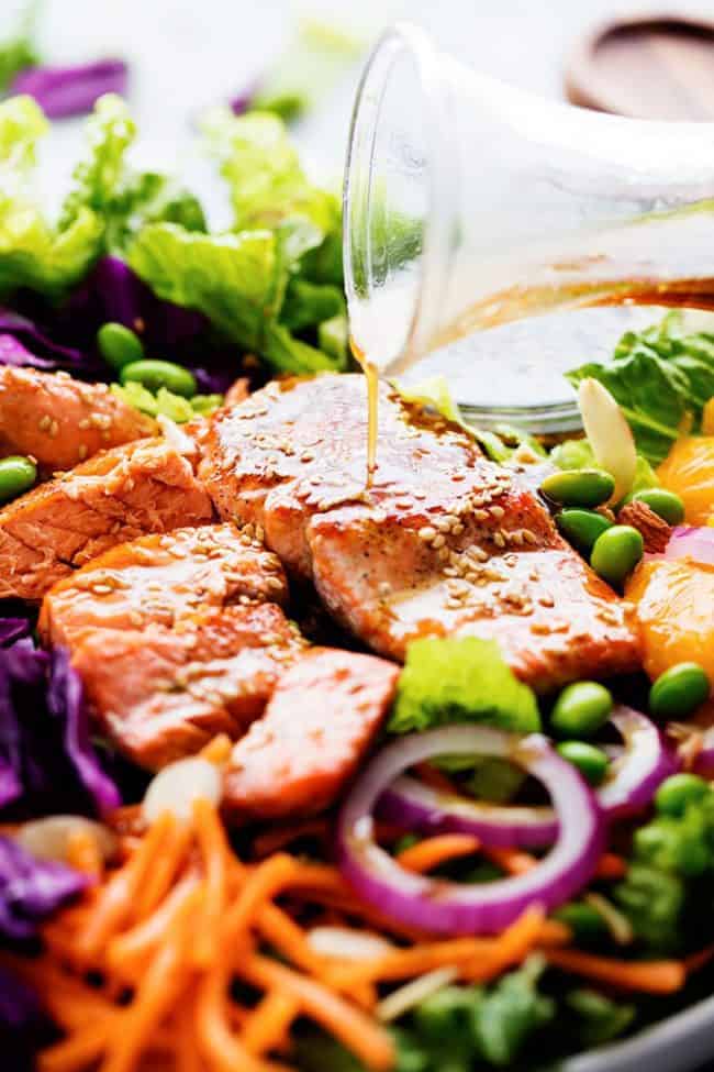 Asian Pan Seared Salmon Salad is bright and vibrant and complete with an amazing honey sesame dressing that takes this salad to a whole new level of delicious! Asian Pan Seared Salmon Salad with dressing being poured over it.