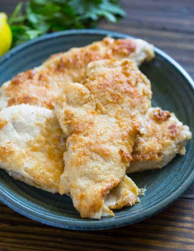 Chicken cooked in creamy garlic lemon sauce is simple and easy to make in one skillet in under 20 minutes! Creamy Lemon Garlic Chicken on a dark blue plate on a wooden table.