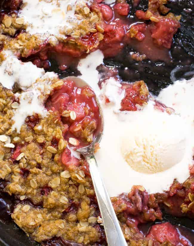 Super Easy Strawberry Crisp. The perfect dessert for summer! Strawberry Crisp in a bowl with a melting scoop of ice cream and a metal spoon.