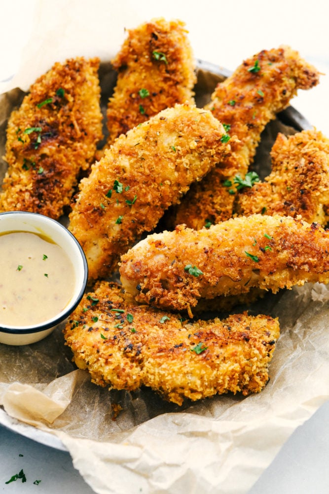 Delicious chicken tenders breaded in a garlic parmesan panko mixture and baked to crispy perfection! This is a meal the entire family will love! Chicken tenders in a basket with honey mustard sauce.