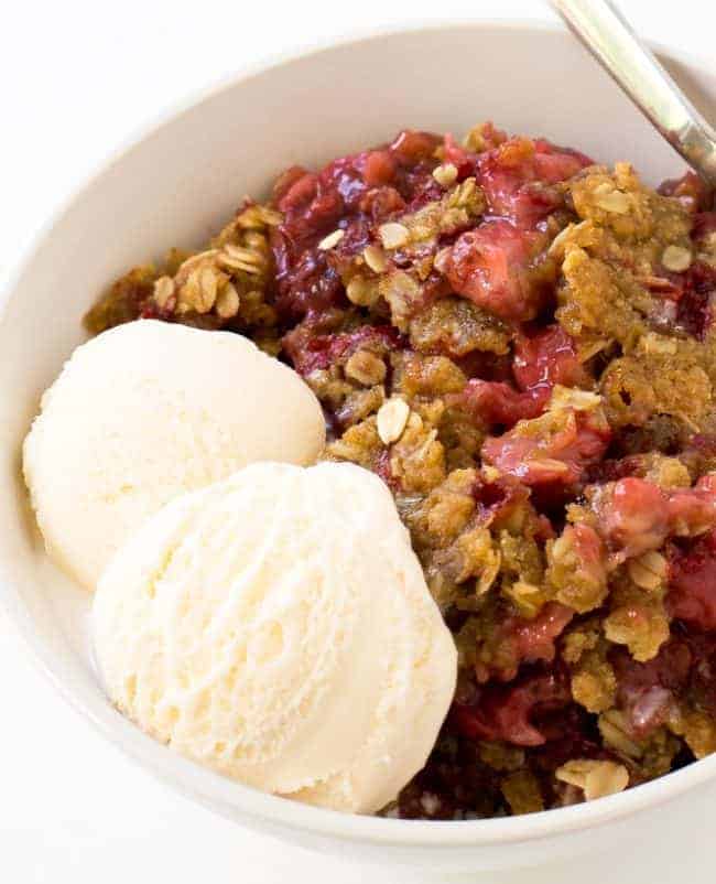 Super Easy Strawberry Crisp. The perfect dessert for summer! Strawberry Crisp in a white bowl with two scoops of ice cream and a metal spoon.