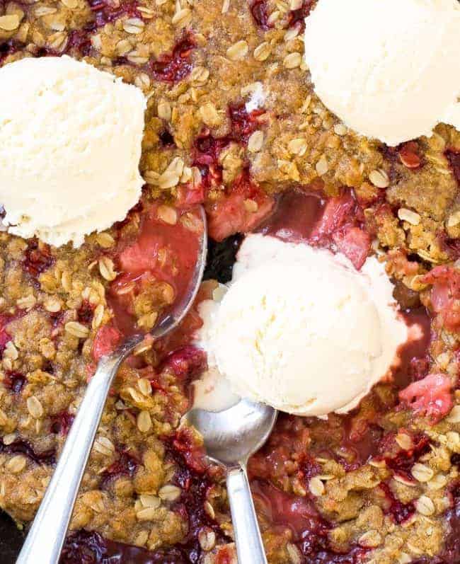 Super Easy Strawberry Crisp. The perfect dessert for summer! Strawberry Crisp with three scoops of ice cream on top with two metal spoons.