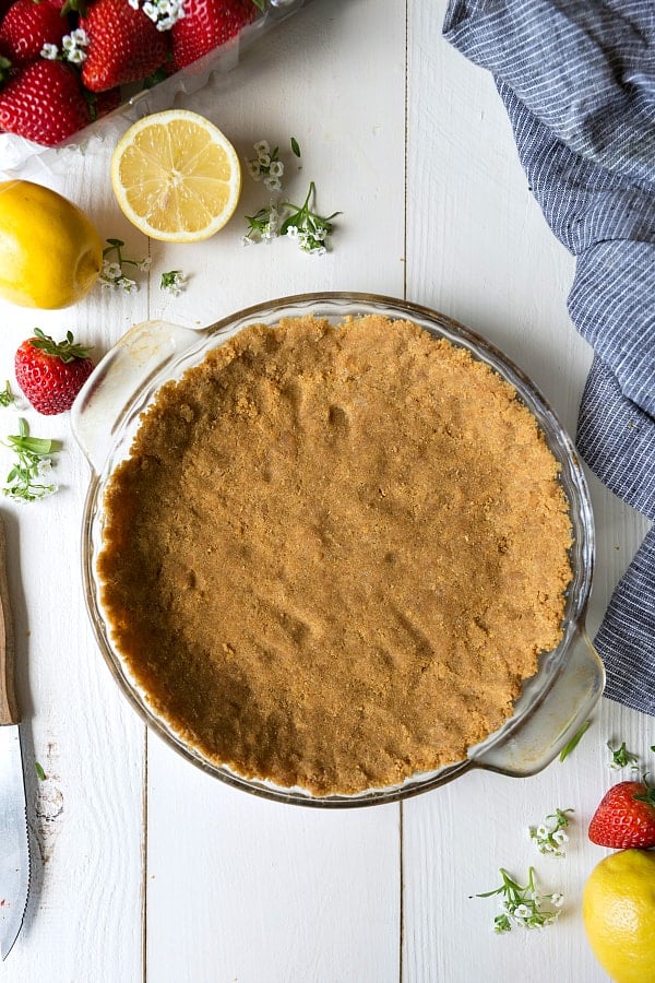 This Easy Lemon Pudding Pie is a creamy & light, slightly tangy, and very refreshing 3 layer dessert!ย Its buttery graham cracker crust is topped with a sweet and tart filling of lemon pudding and whipped cream.ย Insanely delicious and so quick and easy to make! Pie crust in a clear pie pan with fresh lemons and strawberries on the side.