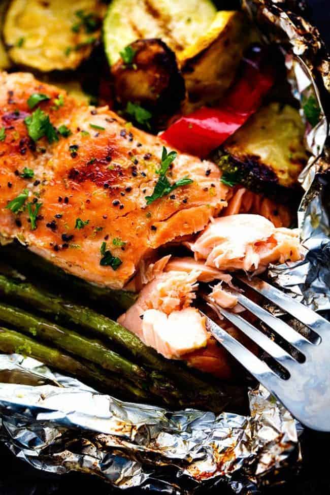 Lime Butter Salmon in Foil with Summer Veggies is grilled to tender and flaky perfection. The foil seals in the lime butter flavor and will be one of the BEST things that you eat! Close up photo of Lime Butter Salmon with a metal fork removing some of the salmon.