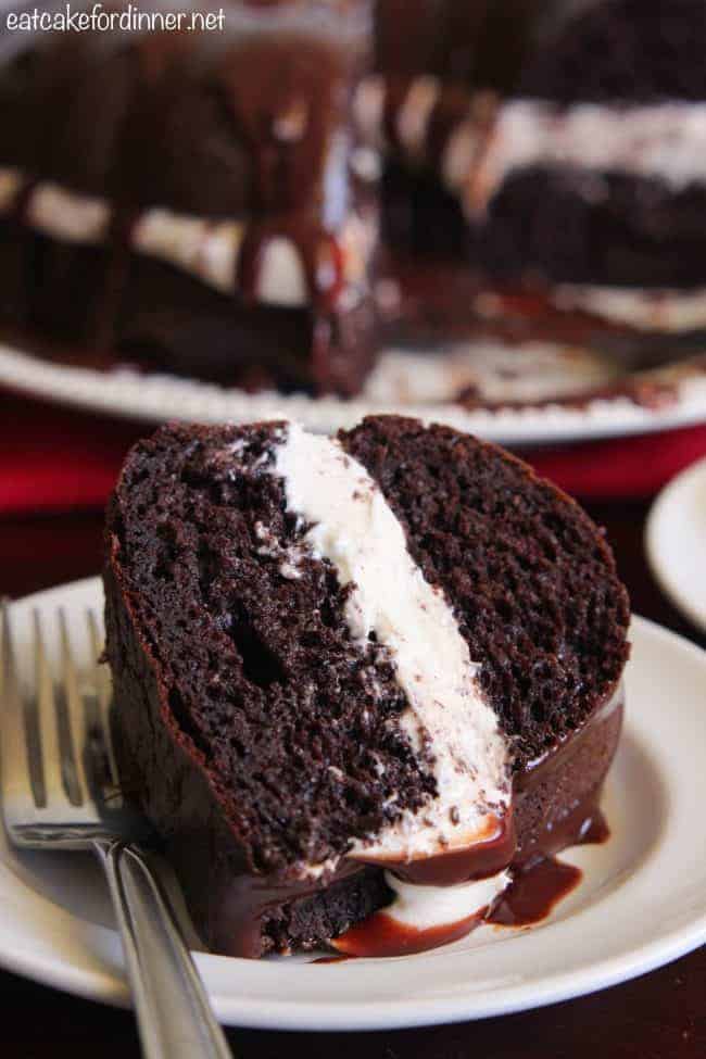 Chocolate Whoopie Pie Cake is a delicious spin on the classic whoopie pie! A dense chocolate cake filled with a soft and pillowy marshmallow filling and drizzled in a chocolate ganache. A slice of Chocolate Whoopie Pie Cake on a white plate with a metal fork.