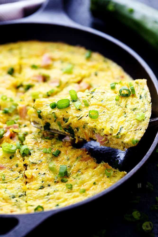 Ham and Cheddar Zucchini Frittata is filled with two cups of zucchini, ham, and cheddar cheese. It has such amazing flavor and will be devoured in no time at all! Ham and Cheddar Zucchini Frittata with a slice being removed from the pan.