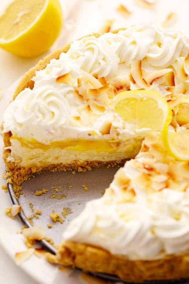 No Bake Lemon Macaroon Cheesecake is a coconut filled cheesecake on top of a golden oreo crust. Topped with lemon curd andย fresh whipping cream this easy to make dessert will be a huge hit! No Bake Lemon Macaroon Cheesecake with a slice removed and a freshly cut lemon in the background.