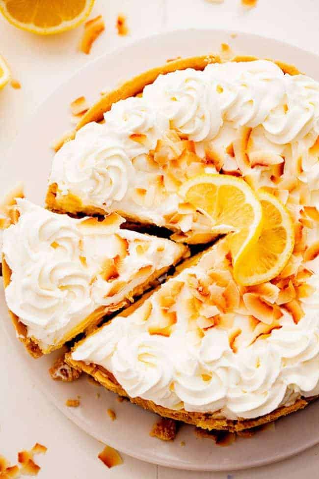 No Bake Lemon Macaroon Cheesecake is a coconut filled cheesecake on top of a golden oreo crust. Topped with lemon curd andย fresh whipping cream this easy to make dessert will be a huge hit! No Bake Lemon Macaroon Cheesecake with a slice being removed.