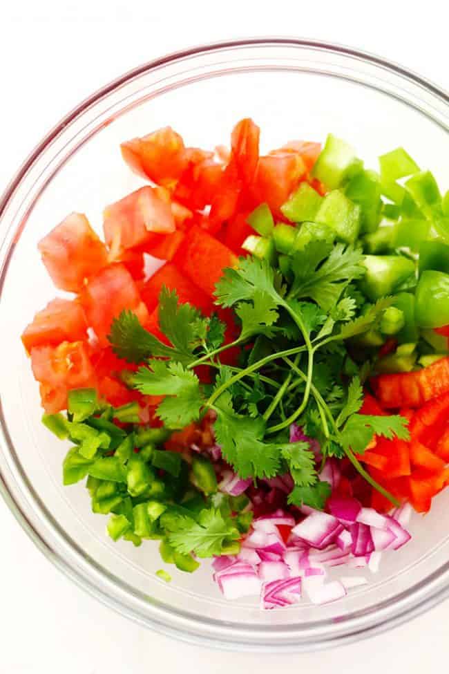 Slow Cooker Restaurant Style Garden Salsa has so many delicious and fresh ingredients and uses up all of those garden tomatoes. It is so addicting you won't be able to get enough! It is also perfect for canning. Ingredients for Slow Cooker Restaurant Style Garden Salsa in a clear bowl.