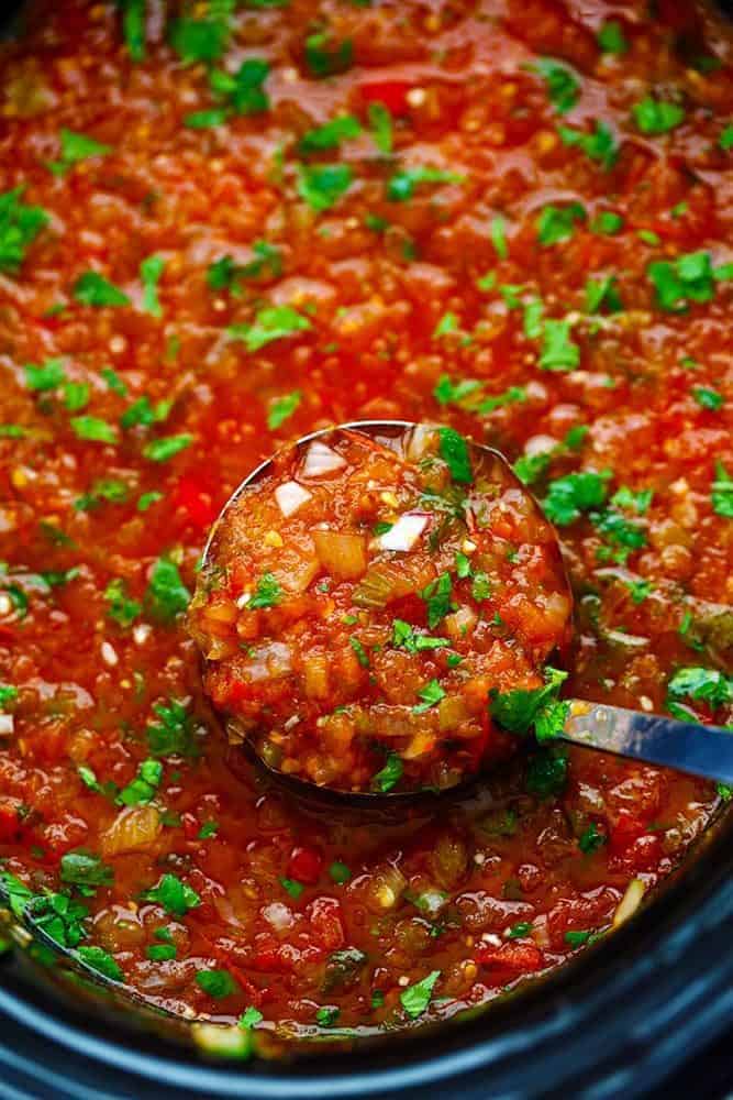 Slow Cooker Restaurant Style Garden Salsa has so many delicious and fresh ingredients and uses up all of those garden tomatoes. It is so addicting you won't be able to get enough! It is also perfect for canning. Restaurant Style Garden Salsa in a slow cooker with a ladle removing some.