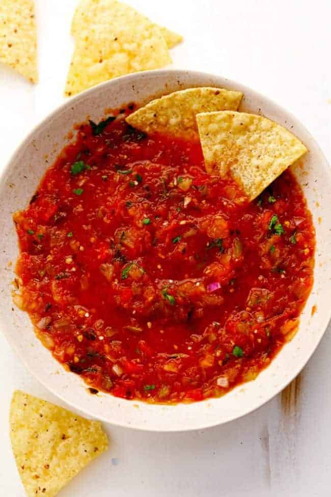 Slow Cooker Restaurant Style Garden Salsa has so many delicious and fresh ingredients and uses up all of those garden tomatoes. It is so addicting you won't be able to get enough! It is also perfect for canning. Slow Cooker Restaurant Style Garden Salsa in a white bowl with tortilla ships on the side.