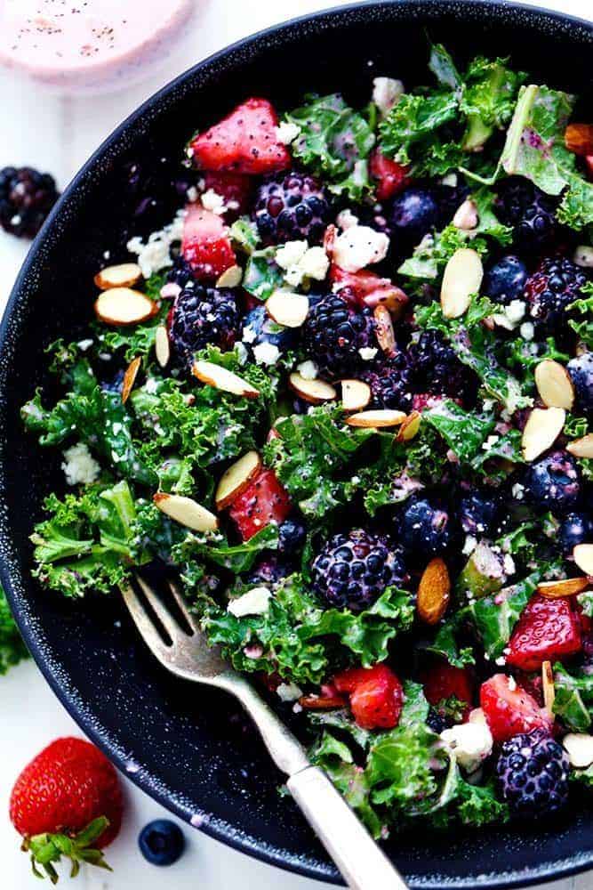 Triple Berry Kale Salad with Creamy Strawberry Poppyseed Dressing is made with delicious fresh summer berries and is tossed with kale, crunchy almonds and topped with feta cheese. A healthy and light salad that is perfect for summer! Triple Berry Kale Salad with Creamy Strawberry Poppyseed Dressing in a black bowl with a metal fork.