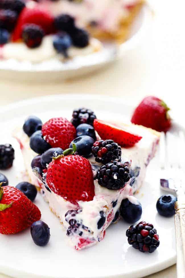 No Bake Very Berry Cheesecake comes together in just 10 minutes! It is filled with fresh summer berries hidden inside a creamy cheesecake and is incredible! A slice of No Bake Very Berry Cheesecake on a white plate with fresh berries on top and on the side.