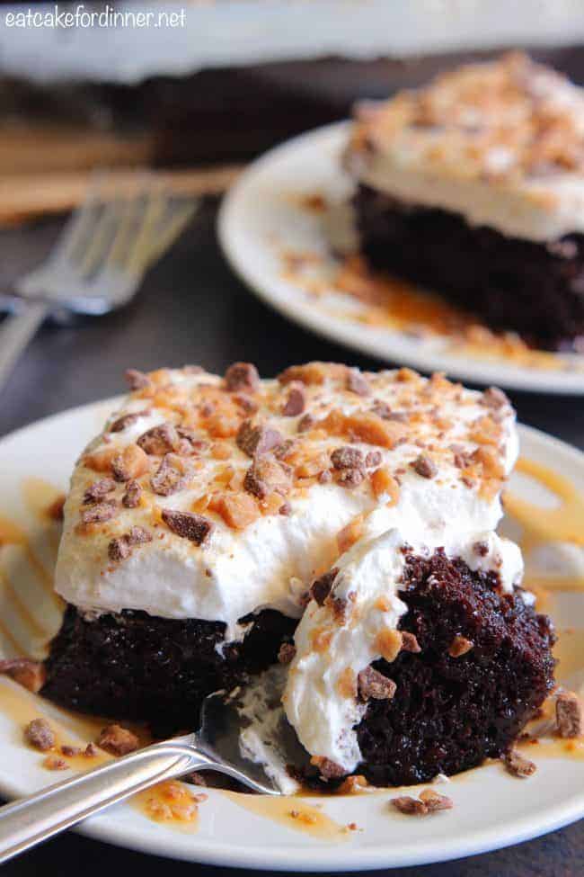Better than Anything Zucchini Poke Cake has caramel inside of a moist chocolate cake. Topped with cool whip and rich toffee bits this will be a HUGE hit! You will never know zucchini is inside!ย Better than Anything Zucchini Cake on a white plate that has a fork taking a bite full out of it.