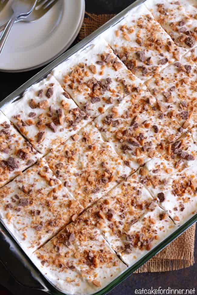Better than Anything Zucchini Poke Cake has caramel inside of a moist chocolate cake. Topped with cool whip and rich toffee bits this will be a HUGE hit! You will never know zucchini is inside!ย Better than Anything Zucchini Cake on a clear cake pan that has been sliced for serving.