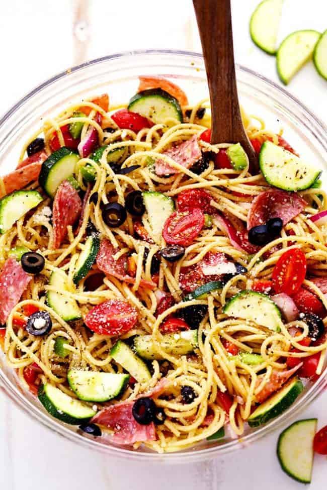 Italian Spaghetti Salad is made with spaghetti, fresh summer veggies, salami and tossed in a homemade zesty Italian dressing. This is a summer potluck must! Italian Spaghetti Salad in a clear bowl and wooden spoon.