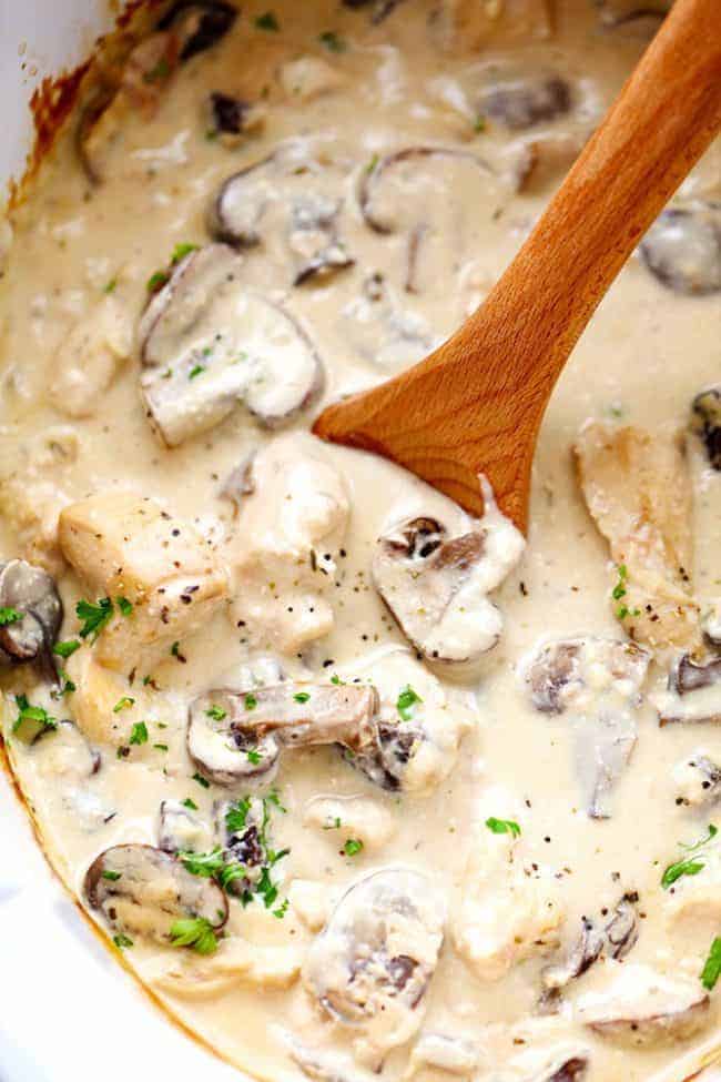 Slow cooker chicken and mushroom stroganoff takes just minutes to throw in the crock pot! It is so creamy and delicious and will become an instant family favorite! Chicken and mushroom stroganoff in a slow cooker with a wooden spoon stirring it.