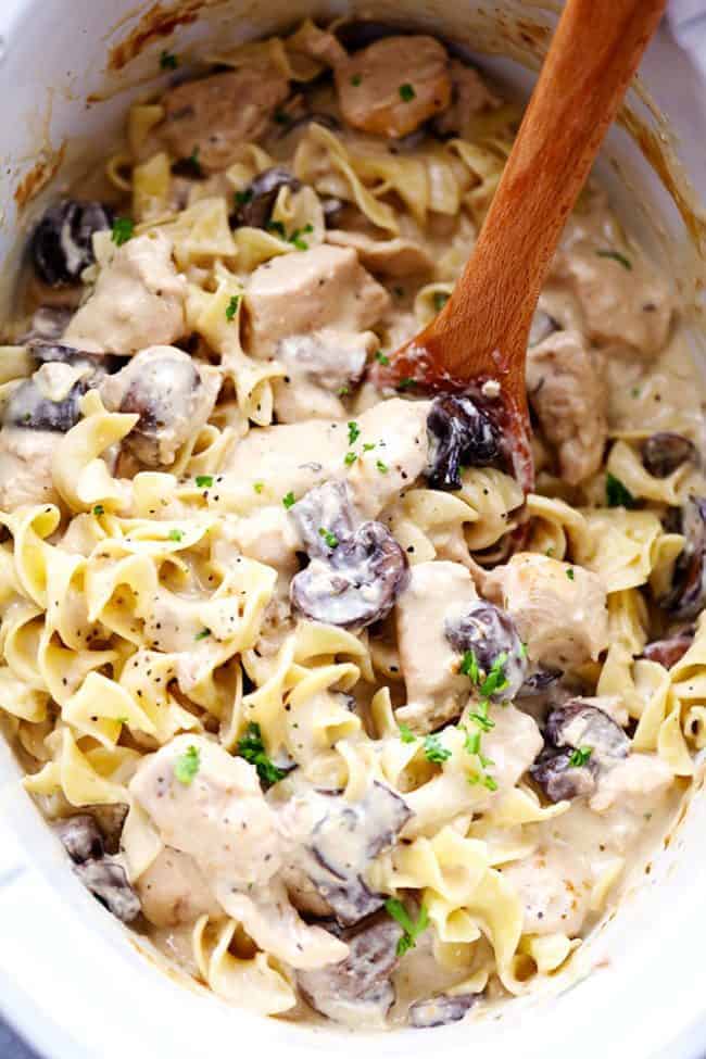 Slow cooker chicken and mushroom stroganoff takes just minutes to throw in the crock pot! It is so creamy and delicious and will become an instant family favorite! Chicken and mushroom stroganoff in a slow cooker being stirred by a wooden spoon.