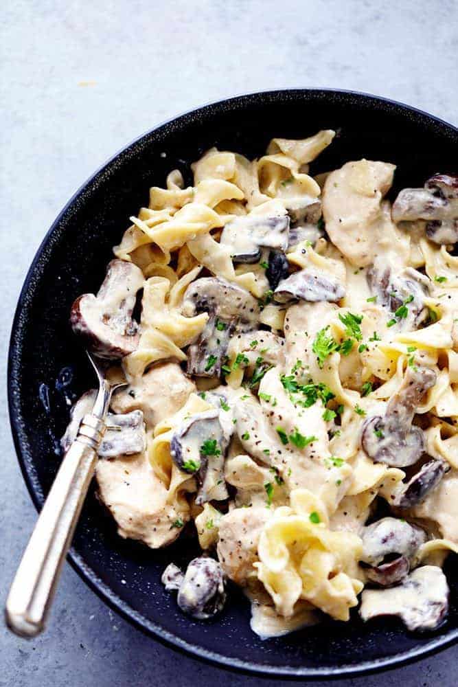 Slow cooker chicken and mushroom stroganoff takes just minutes to throw in the crock pot! It is so creamy and delicious and will become an instant family favorite! Slow cooker chicken and mushroom stroganoff in a black bowl with a fork on the side of the dish.
