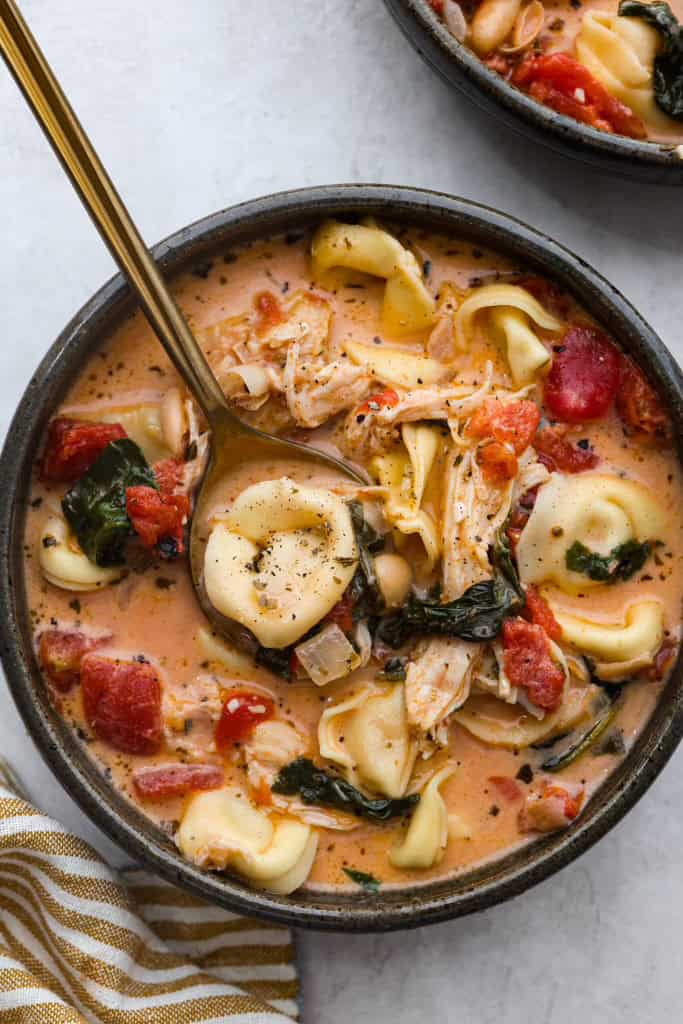 Creamy Tuscan garlic tortellini soup is so easy to make and one of the best soups that you will make! This soup is loaded with cheesy tortellini, diced tomatoes healthy spinach and hearty white beans. This soup is so creamy and delicious, I know your family will love it! Overhead shot of a bowl of creamy Tuscan garlic tortellini soup.